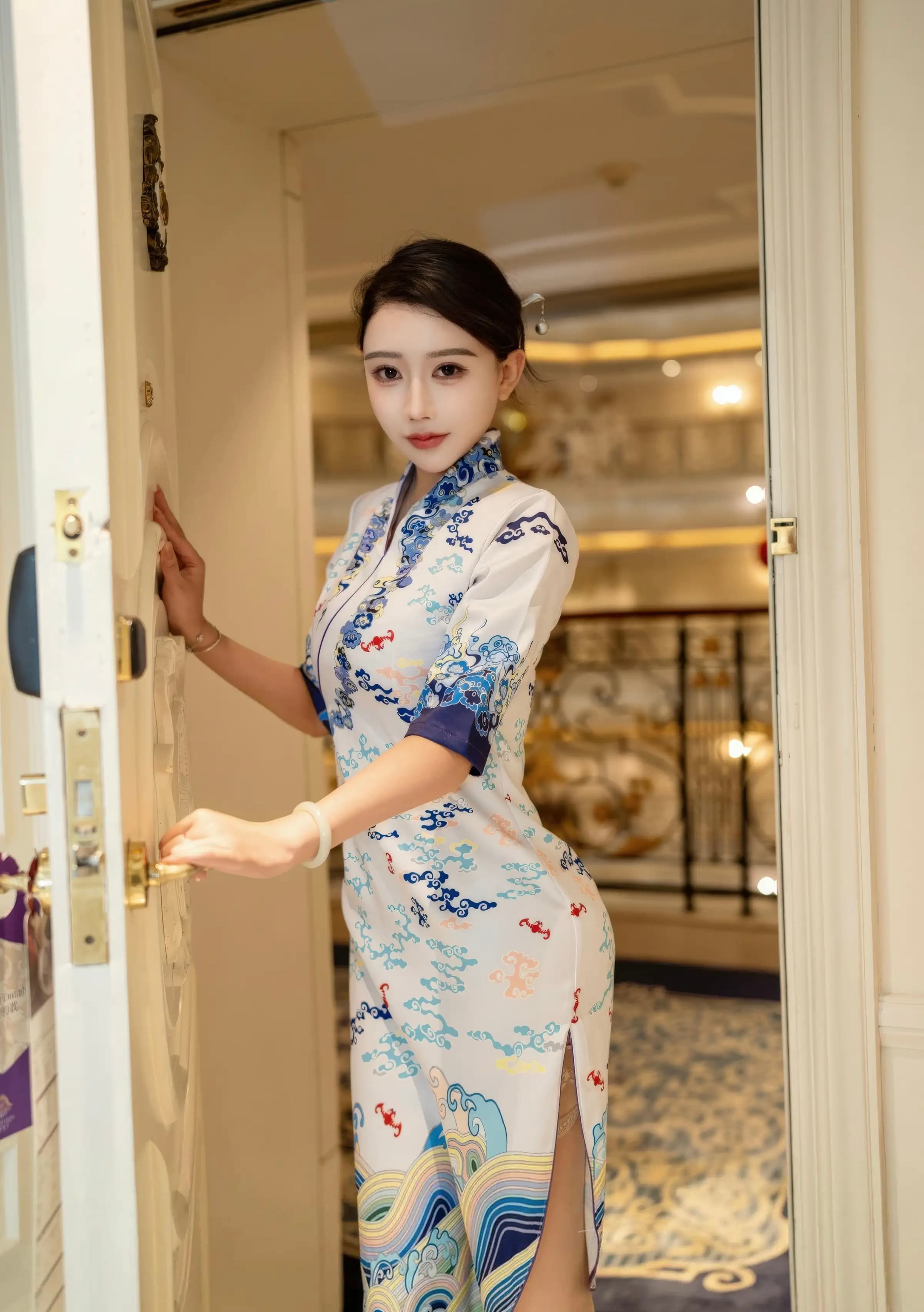 Woman in a white patterned cheongsam stands in a doorway, holding a gold door handle.